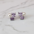 Pair of earrings with purple and pearl stones on a light surface.