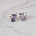 Pair of earrings with purple and pearl stones on a light surface.