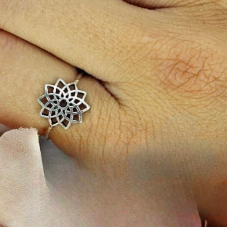 A sterling silver flower ring on a person's finger, displaying intricate detailing and a shiny finish.