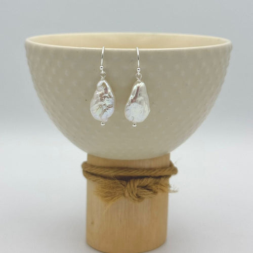 Beige bowl with teardrop-shaped earrings on a wooden stand against a light gray background