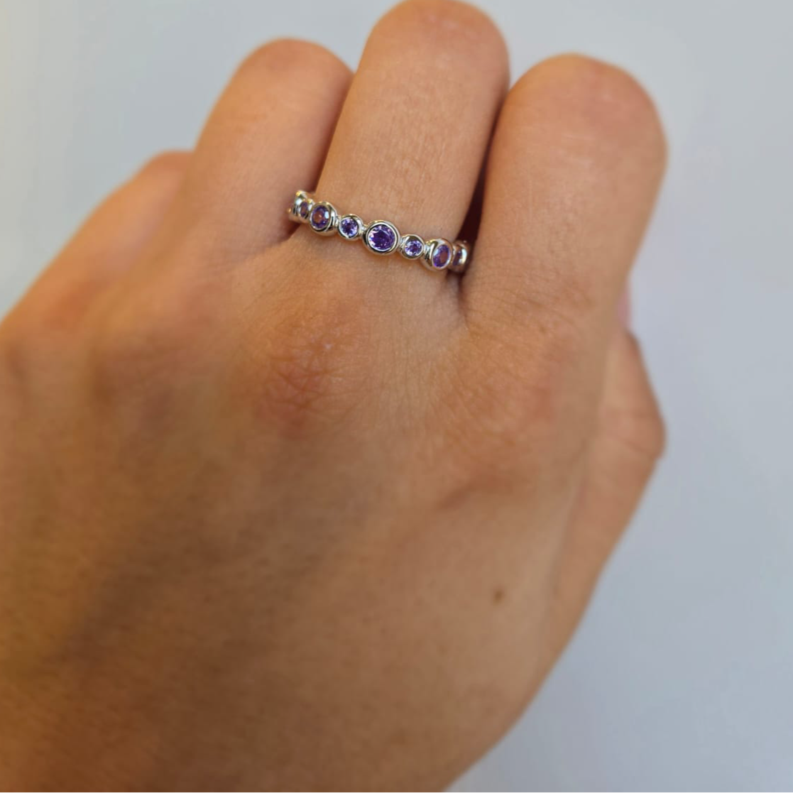 A purple cubic zirconia eternity ring on a person's hand, showcasing the band with multiple purple stones set in the metal.
