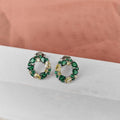 Pair of green gemstone earrings on a white surface with a pink fabric background