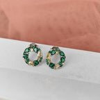 Pair of green gemstone earrings on a white surface with a pink fabric background
