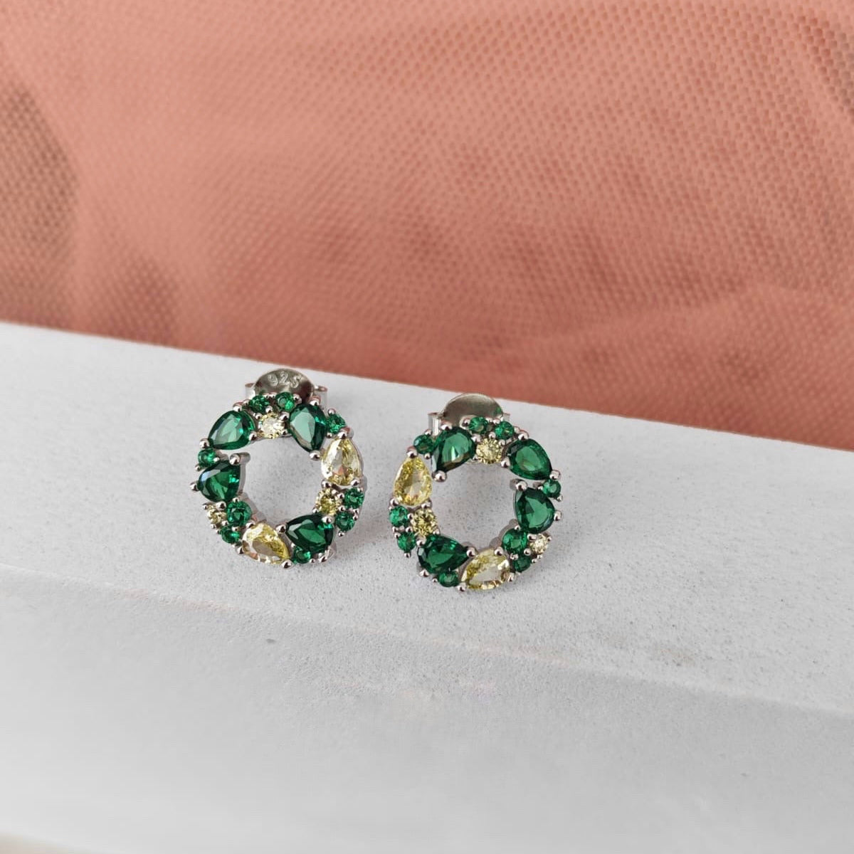 Pair of green gemstone earrings on a white surface with a pink fabric background