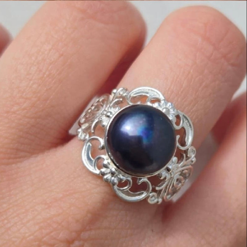 Silver ring with a dark gemstone on a finger