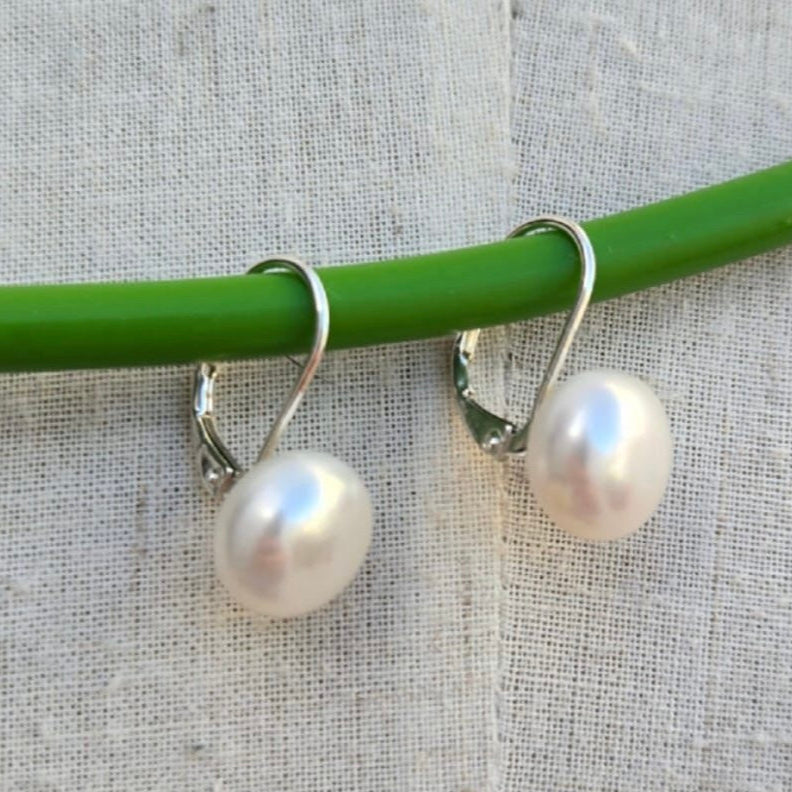 Pearl earrings hanging from a green rod on a textured gray background