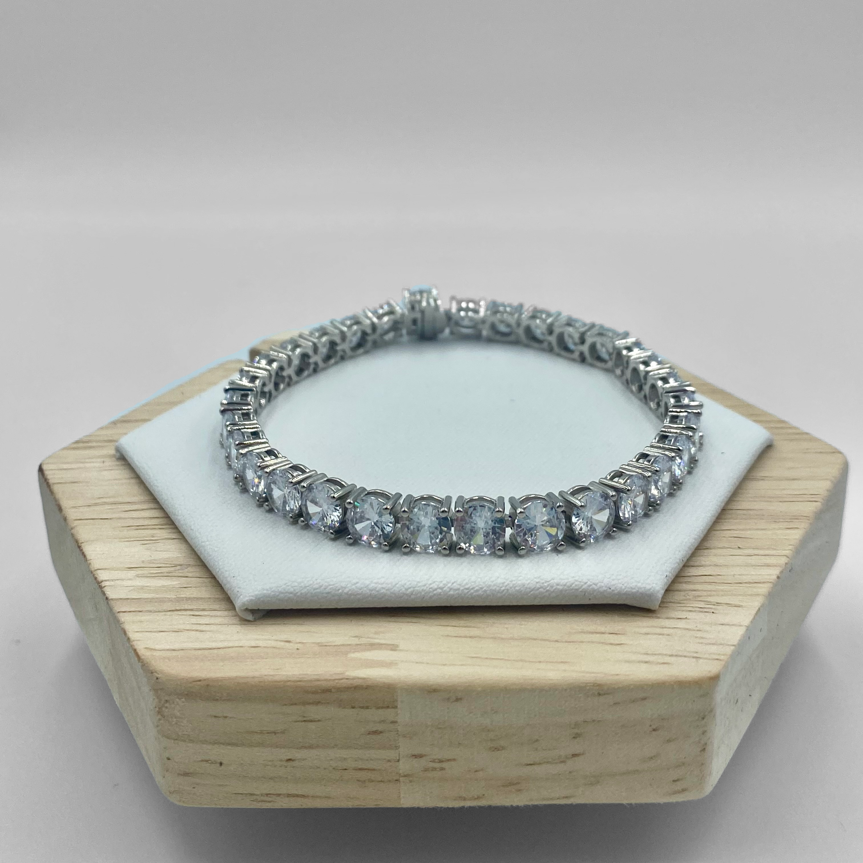 A sterling silver tennis bracelet with 5mm cubic zirconia beads and a secured clasp, displayed on a wooden stand.