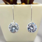 Silver earrings with clear gemstones in front of a plant pot.