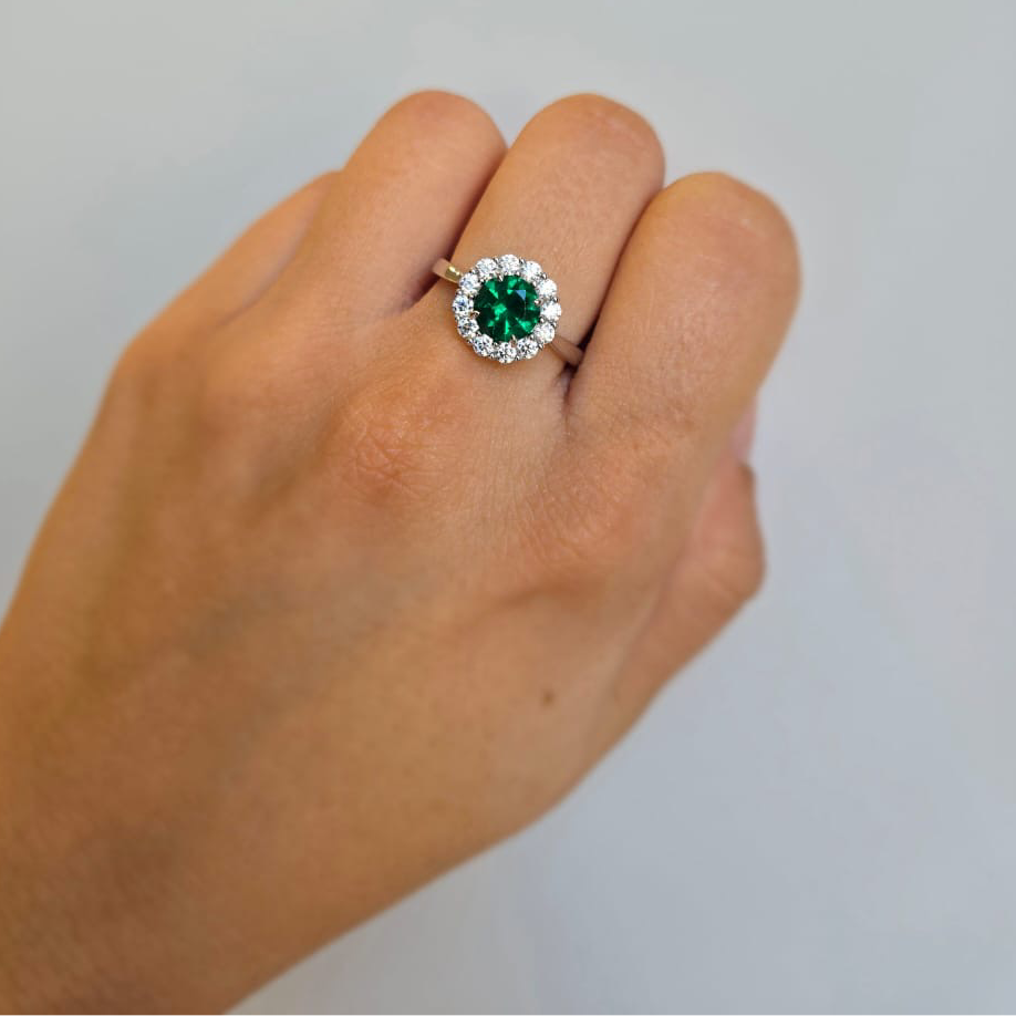 A sterling silver ring with a green cubic zirconia stone surrounded by a white stone edge, worn on a person's finger.