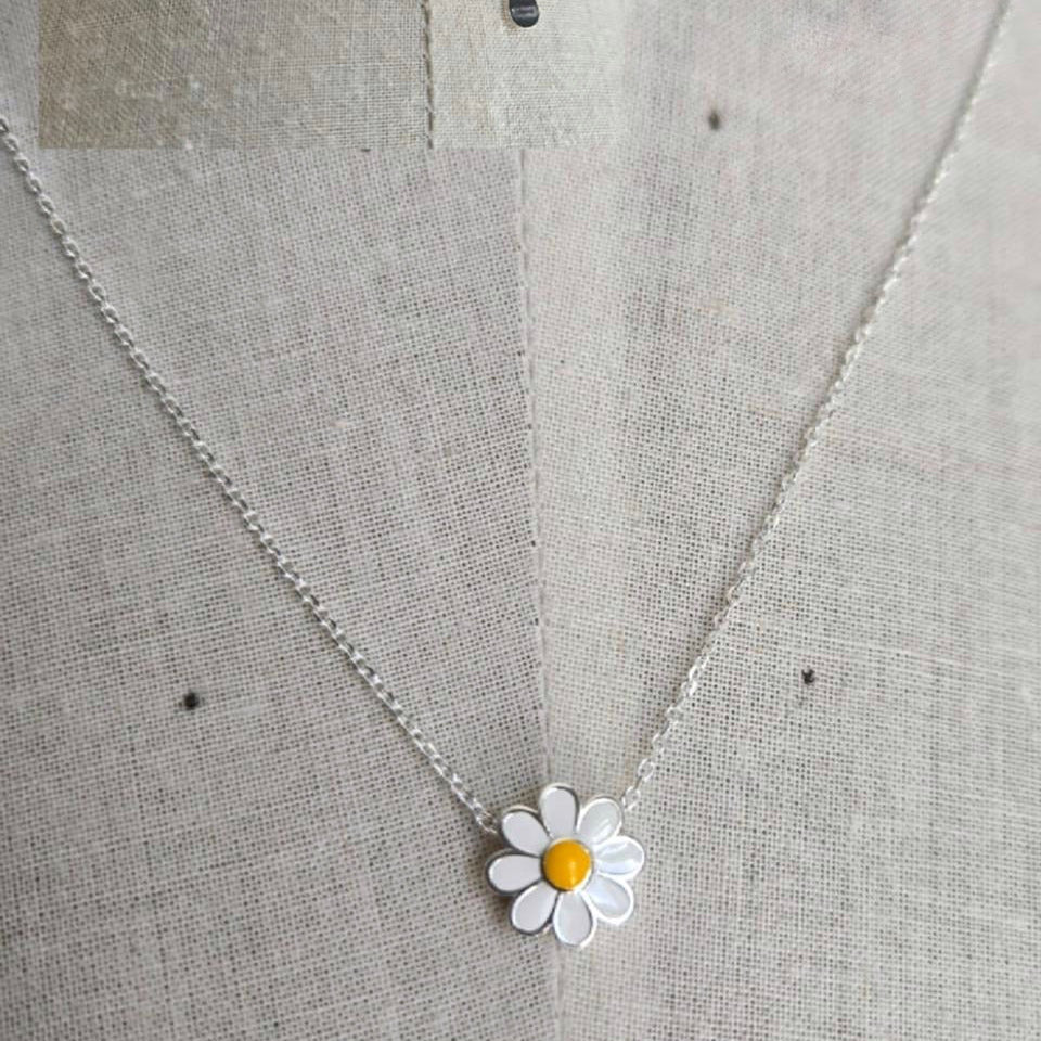 Silver necklace with a daisy pendant on a textured fabric background