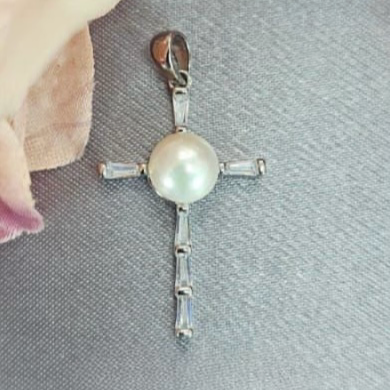 A sterling silver cross pendant featuring a cubic zirconia stone and a freshwater pearl detail, displayed against a neutral background.