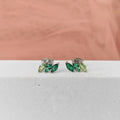 Pair of green gemstone earrings on a white surface with a pink fabric background