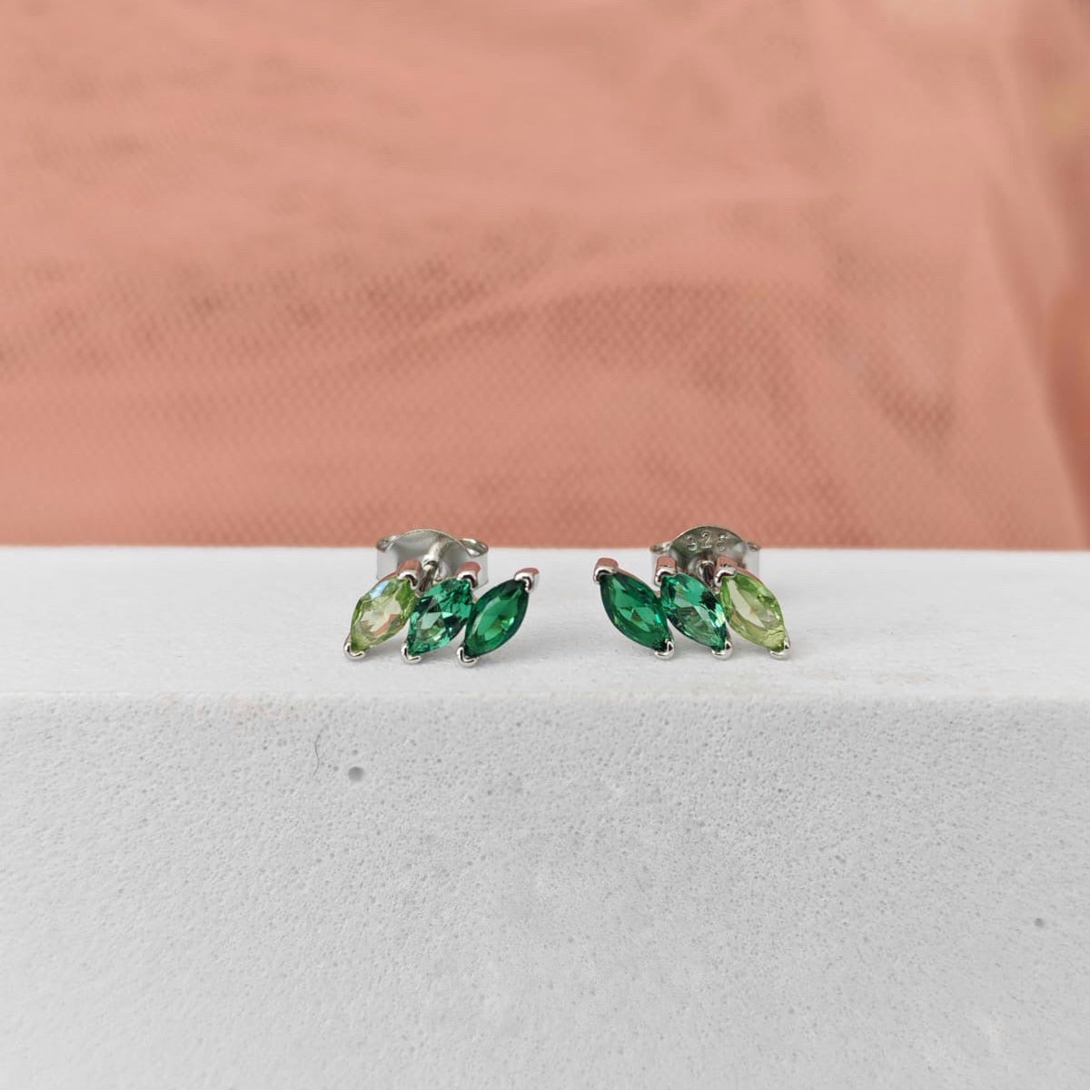 Pair of green gemstone earrings on a white surface with a pink fabric background
