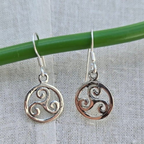 Silver triskele earrings hanging on a green rod against a light fabric background