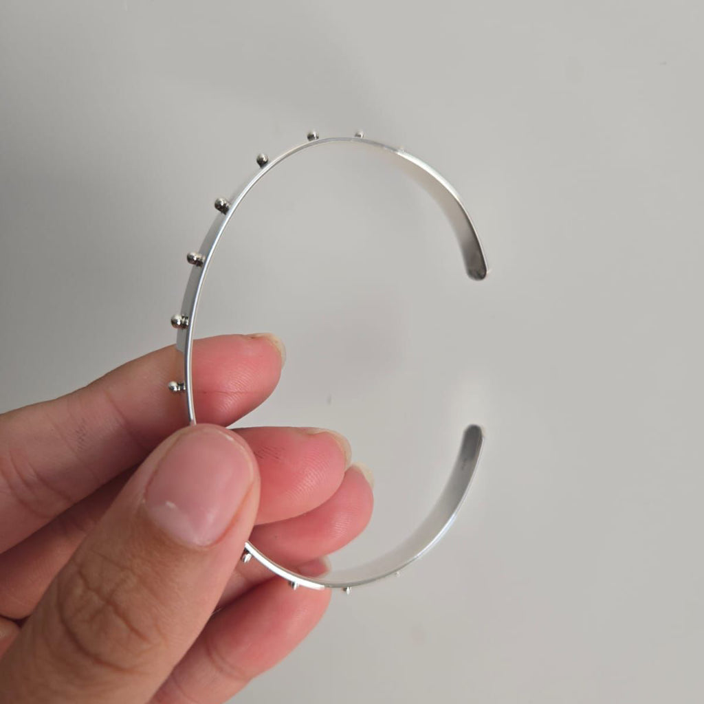 Silver headband held by a hand against a plain background