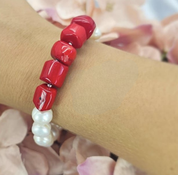 A bracelet featuring red coral semi-precious stone and freshwater pearl beads on an elastic band, displayed on a person's wrist.