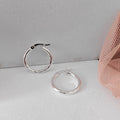 Silver hoop earrings on a light gray surface with a pink mesh fabric in the background