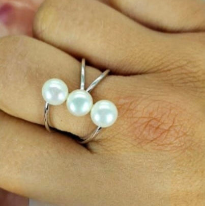 A sterling silver ring with three freshwater pearls in a row and cross silver bands, displayed on a person's finger.