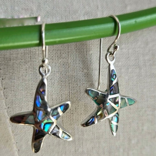 Star-shaped earrings with abalone inlay on a green stick against a gray background