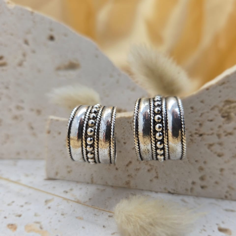 Silver cylindrical earrings on a textured surface with a blurred background
