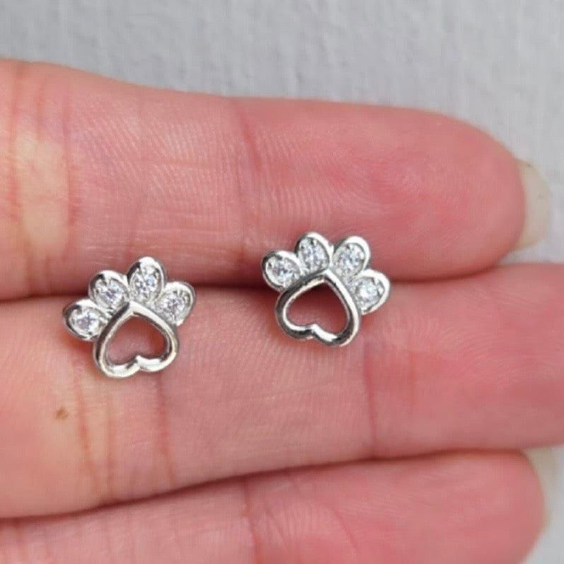 Silver paw print earrings with clear stones held between fingers on a light background