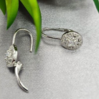 A pair of sterling silver drop earrings with cubic zirconia, displayed on a fabric surface with a green leaf in the background.