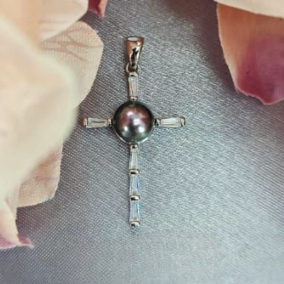 A silver pendant featuring a blue freshwater pearl and cubic zirconia stones, displayed against a backdrop with peach tones.