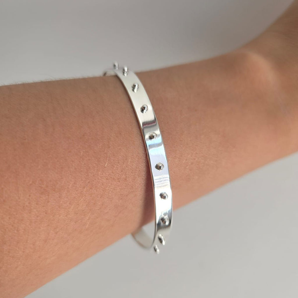 Silver bracelet on a person's wrist against a neutral background