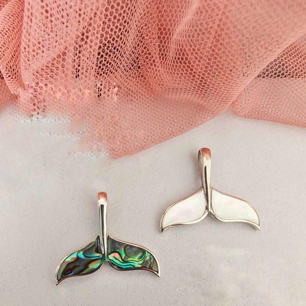 Mermaid tail earrings on a white surface with pink fabric in the background