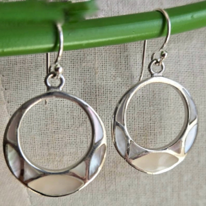 Silver hoop earrings hanging on a green rod with a neutral background