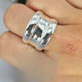 A person's hand wearing a sterling silver statement ring with a reflective surface.
