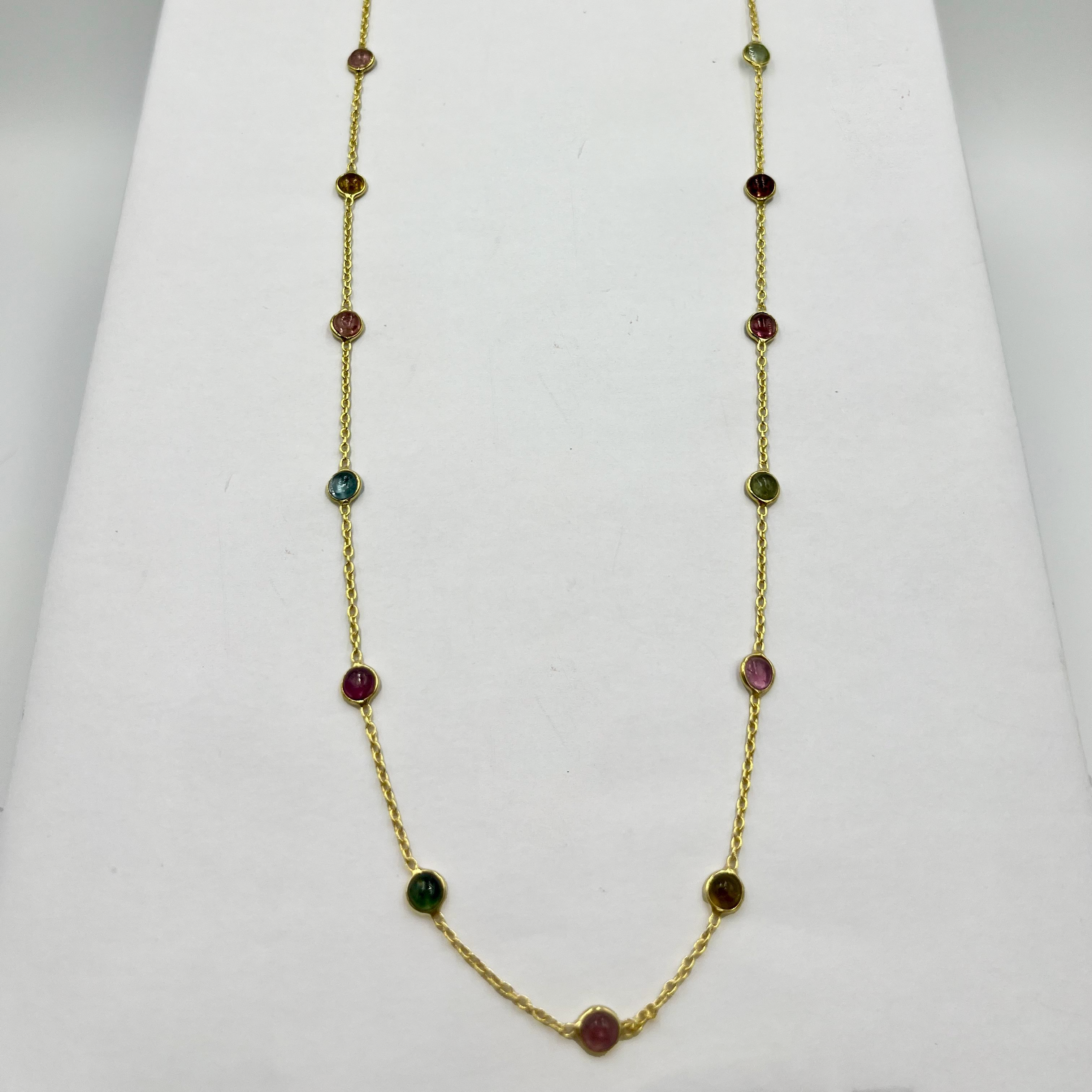 A gold chain necklace with semi-precious tourmaline stone drops displayed on a white stand.