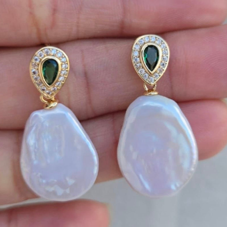 Pearl earrings with green gemstones held between fingers