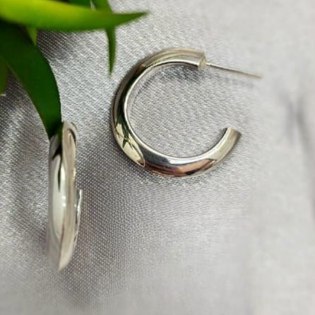 A pair of sterling silver hoop earrings on a linen surface.