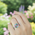 A sterling silver ring with a circular design containing multicolored gemstones, displayed on a person's finger.