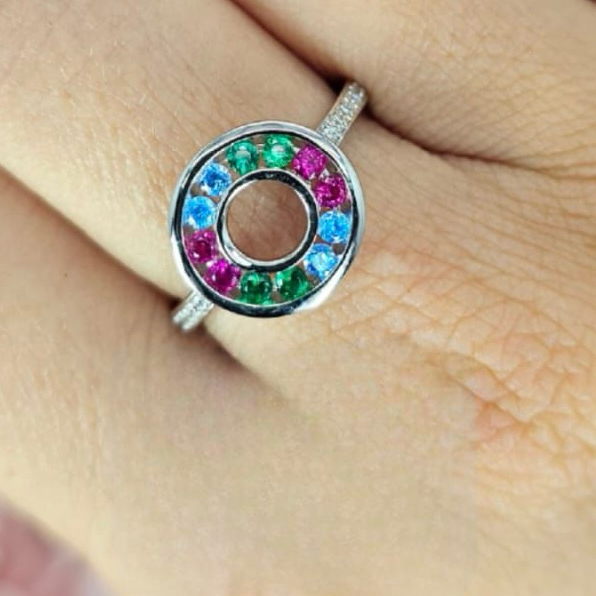 A sterling silver ring with a circular design containing multicolored gemstones, displayed on a person's finger.