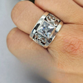 A sterling silver ring with intricate filigree designs and a square cubic zirconia center stone held on a human hand.