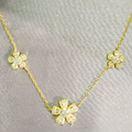 A gold necklace with three flower pendants, each adorned with what appears to be cubic zirconia stones, displayed against a grey background.