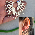 Silver leaf-shaped earrings held in hand with close-up of ear wearing one.