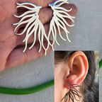 Silver leaf-shaped earrings held in hand with close-up of ear wearing one.