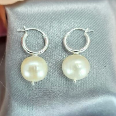 A pair of silver hoop earrings featuring an 11mm freshwater pearl on each hoop, displayed on a grey fabric surface.