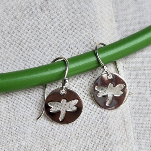 Dragonfly-themed silver earrings on a green stick against a textured fabric background