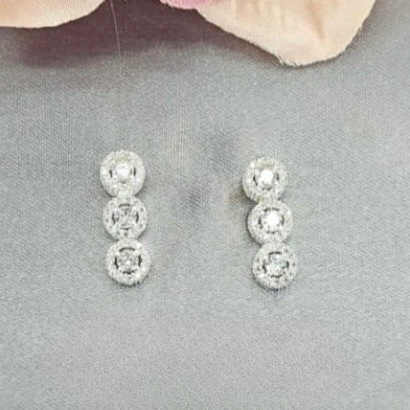 Pair of silver earrings on a gray surface with a pink flower in the background