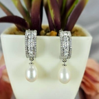 Sterling silver drop earrings with cubic zirconia detail and freshwater pearl on end, displayed in a white vase with a green plant background.