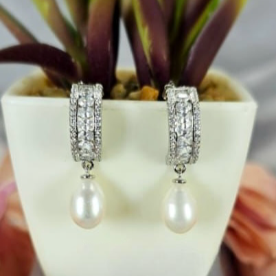 Sterling silver drop earrings with cubic zirconia detail and freshwater pearl on end, displayed in a white vase with a green plant background.