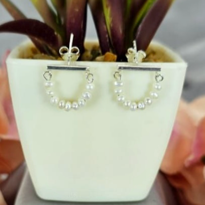 A pair of silver stud earrings featuring tiny freshwater pearls set in a halfmoon shape on a bar, displayed in a white vase with green leaves.