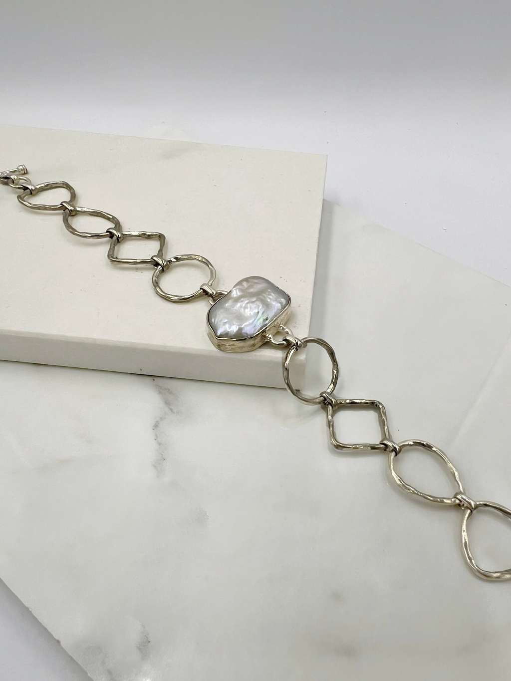A sterling silver bracelet with large links and a single pearl in a tube setting, displayed on a white surface.