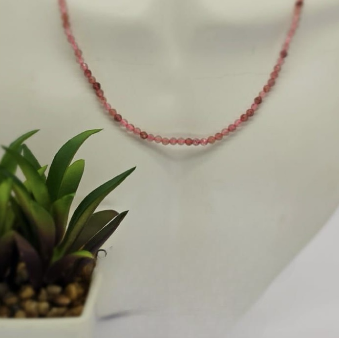 A Strawberry Quartz semi precious stone necklace displayed on a mannequin's neck, with a sterling silver clasp, alongside a potted plant.