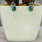 A pair of sterling silver cubic zirconia cluster stud earrings displayed in front of a white plant pot.