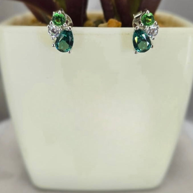 A pair of sterling silver cubic zirconia cluster stud earrings displayed in front of a white plant pot.